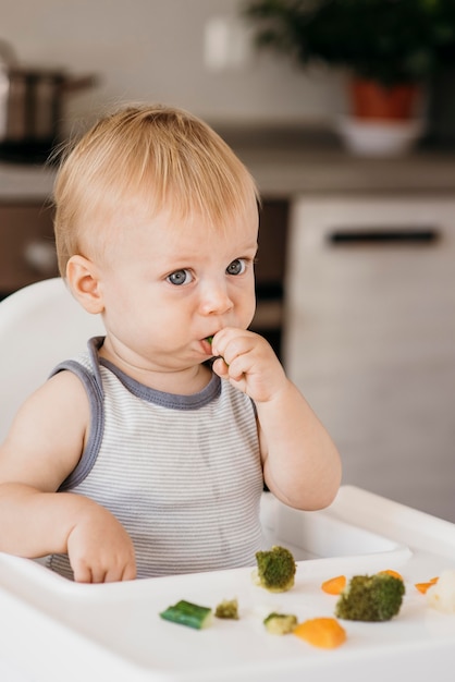 Baby boy in highchair eating vegetables