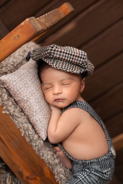 Baby boy newborn infant sleeping on brown wooden bed in little suit and hat