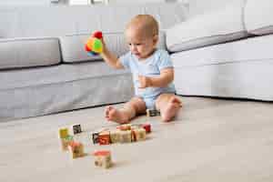 Foto gratuita neonato che si siede sul pavimento e giocare con i giocattoli in salotto