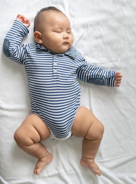 A baby boy in a striped shirt is sleeping in bed.