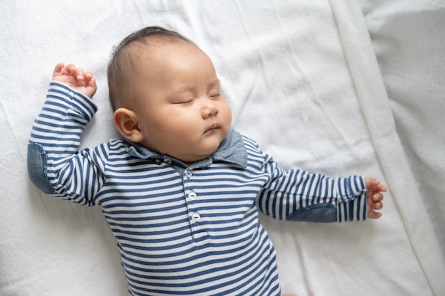 A baby boy in a striped shirt is sleeping in bed.