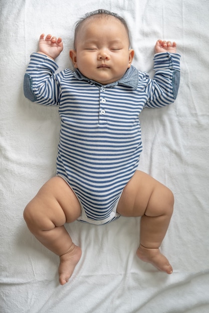 Free photo a baby boy in a striped shirt is sleeping in bed.