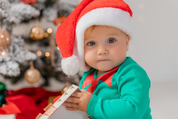 Baby in christmas gnome costume opens gifts near christmas tree products for children and holidays