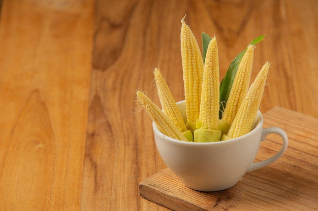 Baby corn is placed in a glass on a wooden floor.