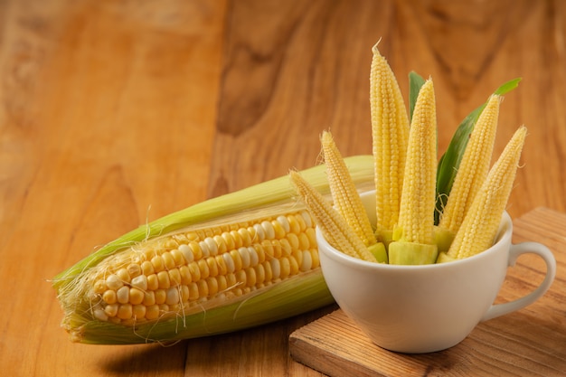 Baby corn is placed in a glass on a wooden floor.