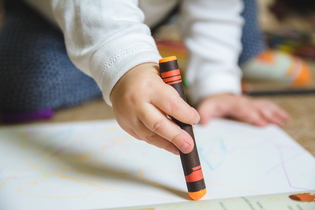Baby drawing with an orange crayon on the paper