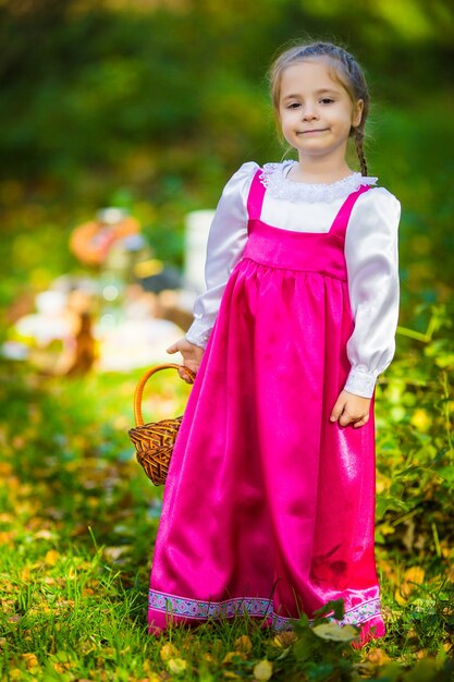 Baby girl in costumes of Masha from cartoon Masha and Bear on autumn forest
