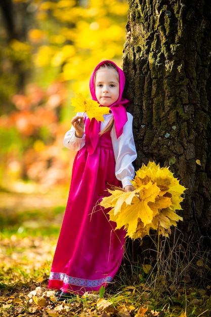 Baby girl in costumes of Masha from cartoon Masha and Bear on autumn forest