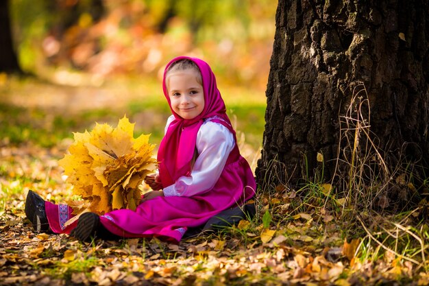 Baby girl in costumes of Masha from cartoon Masha and Bear on autumn forest