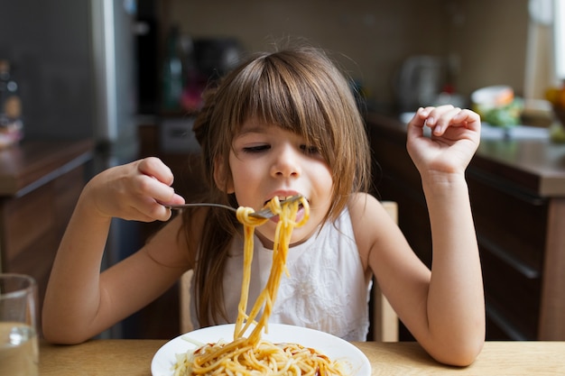 屋内のパスタ料理を持つ女の赤ちゃん