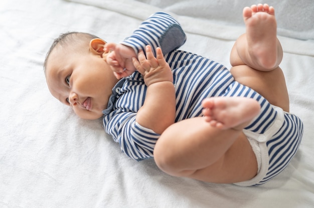 Free photo the baby is lying on his back and his hands and feet are raised on the white bed.