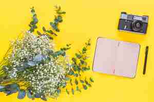 Бесплатное фото Дыхательные цветы; дневник; ручка и винтажная камера на желтом фоне