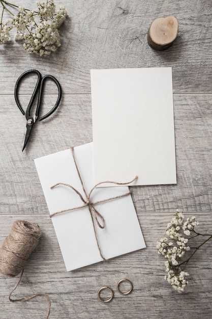 Baby's-breath flowers; miniature tree stump; scissor; spool and wedding rings on wooden background