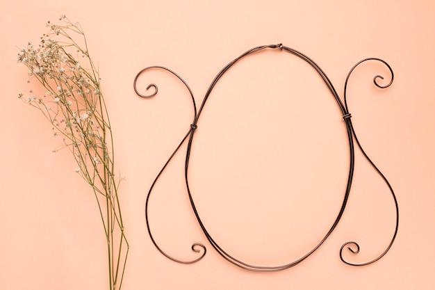 Free photo baby's breath flowers near the empty oval frame on peach colored backdrop