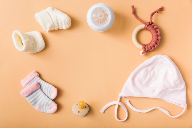 Baby's sock; pair of woolen shoes; pacifier; cap; milk bottle; toy on an orange background