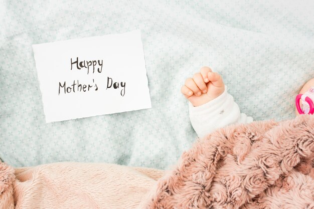 Baby sleeping in bed near Happy Mothers Day inscription 