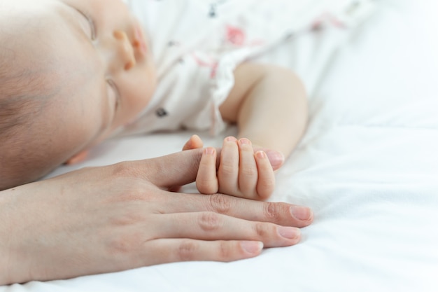 寝ている母親の指をつかんでいる赤ちゃん