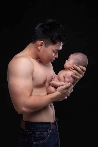 The baby sleeps in the hands of a strong father.