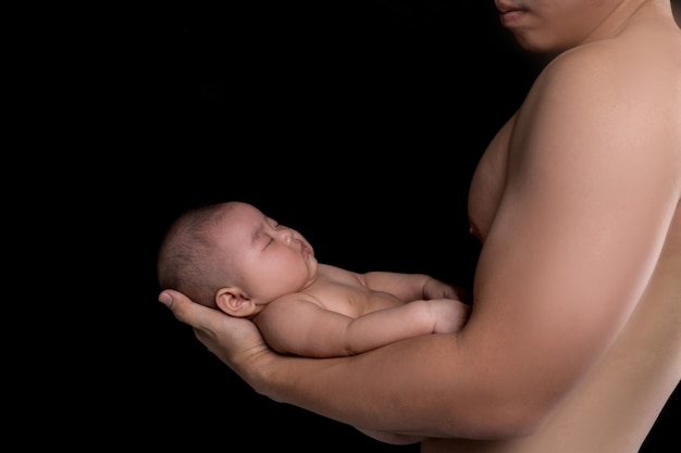 The baby sleeps in the hands of a strong father.