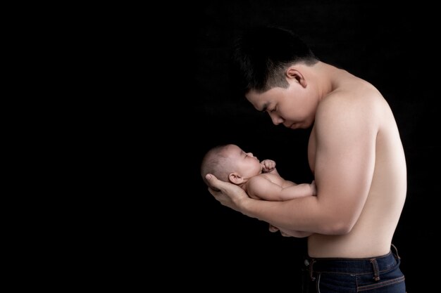 The baby sleeps in the hands of a strong father.