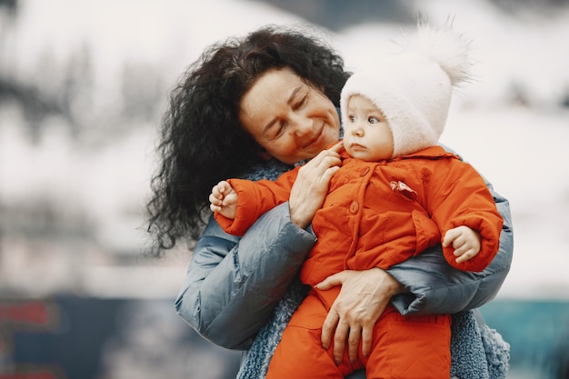 Baby in warm clothes. Grandmother standing with her granddaughter. Vacation in the mountains in winter