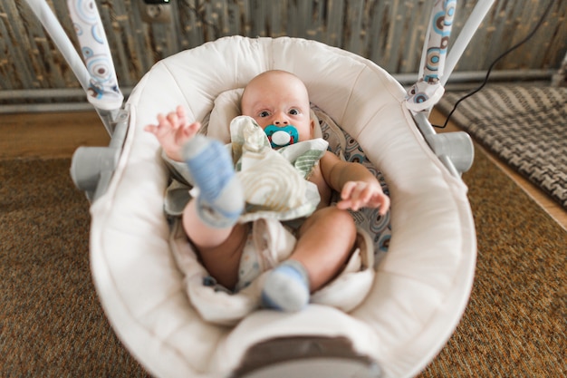 Baby with pacifier lying on baby carriage at home