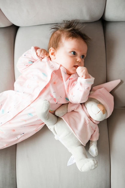 Baby with toy lying on couch at home