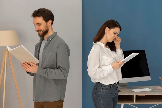 Спиной к спине мужчина с книгой и женщина с планшетом