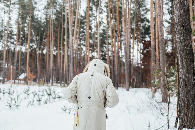Спина человека в зимнем пальто идет в снежный лес