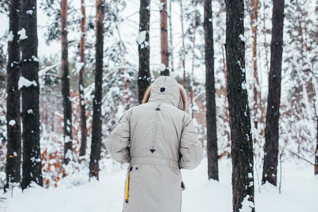 겨울 코트를 입은 남자가 눈 숲으로 걸어갑니다.