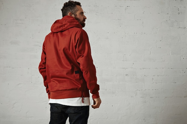 Back portrait of a stylish bearded guy wearing a brick red anorak, black jeans and white t-shirt isolated on white