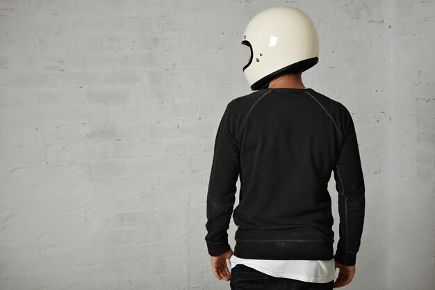 Back portrait of a young man dressed in black and white casual clothes wearing a shiny white blank motorcycle helmet isolated on white