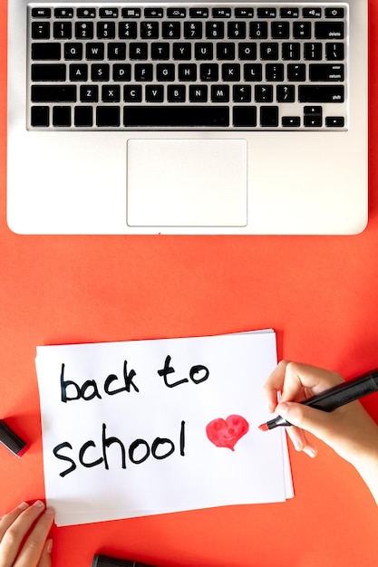 Foto gratuita torna a scuola la mano del bambino scrive su un foglio su uno sfondo rosso