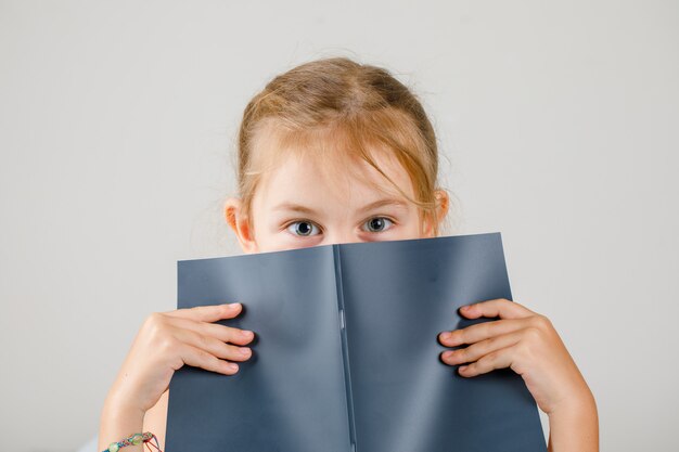 Back to school concept side view. girl hiding her face with copybook.