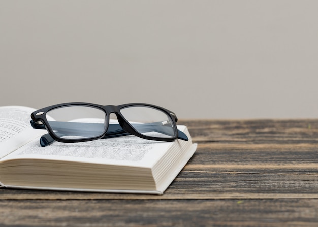 Back to school concept with glasses on book on wooden and white wall side view.