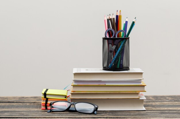 Back to school concept with glasses, school items on wooden and white wall side view.