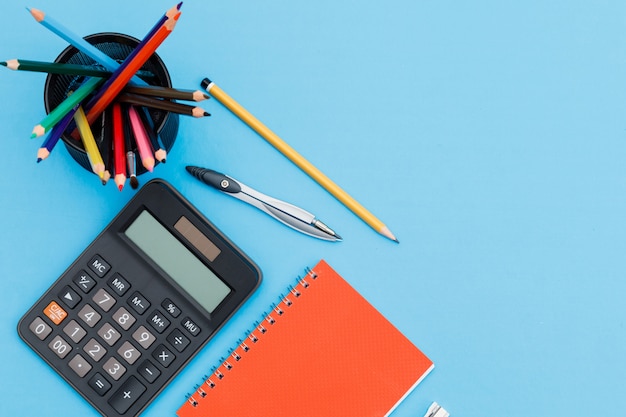 Back to school concept with notebook, pencils, calculator, compass on blue background flat lay.