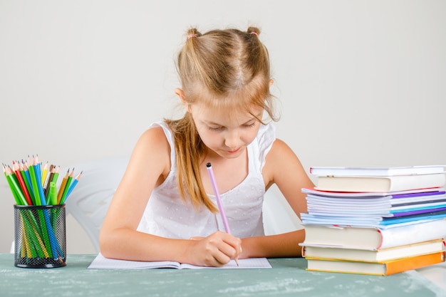 back to school concept with pencils, books side view. little girl writing on copybook.