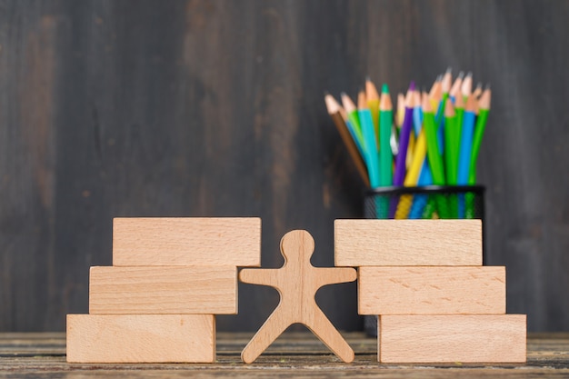 Free photo back to school concept with wooden blocks, human figure, pencils on wooden table side view.