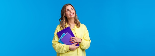 Снова в школу симпатичная блондинка улыбающаяся европейская студентка носит тетради и смотрит учебный материал