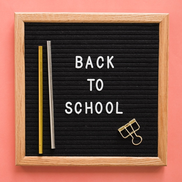 Back to school text on slate with pencils and bulldog clip on colorful backdrop