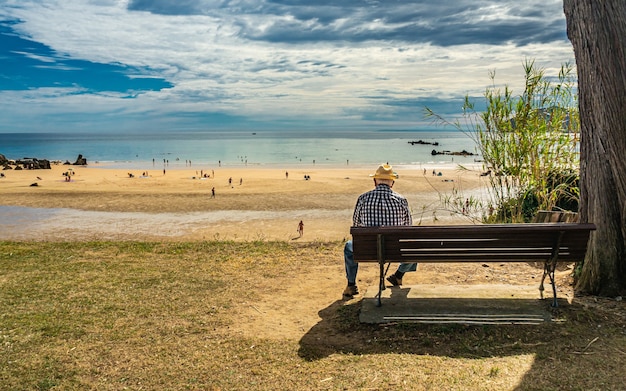 Back of a senior male sitting on a bench on the coast of the sea