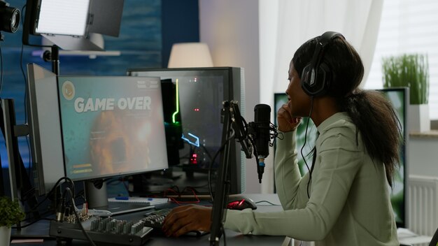 Back shot of afro american esport streaming losing virtual competition wearing headphones. Professional gamer streaming online video games with new graphics on powerful computer.