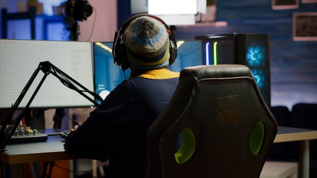 ホームスタジオでRGBキーボードを使用して一人称ビデオゲームをプレイするプロゲーマー女性のバックショット。オンライン競争中にプロのゲーム強力なコンピューターを使用してゲームプレイをストリーミングするゲーマー