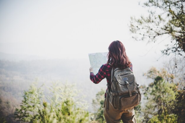Задняя сторона девушки-путешественника, которая ищет правильное направление на карте, путешествуя пешком по горам. Концепция путешествия.