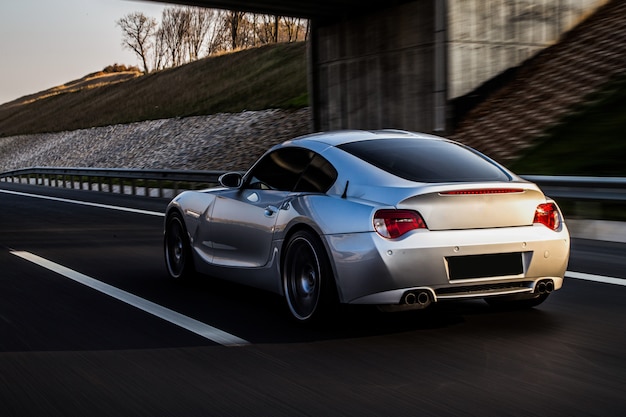 Back and side view of a metallic silver coupe on the road.