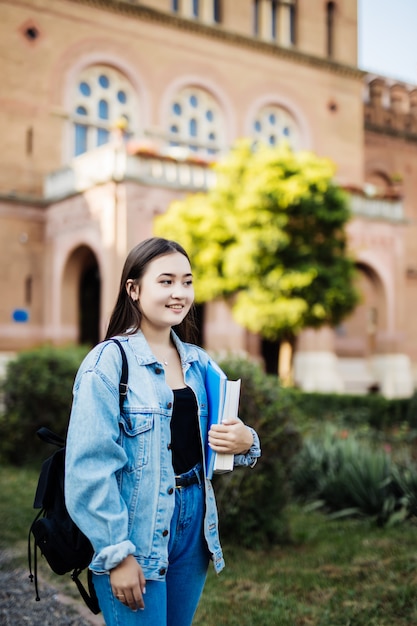 Бесплатное фото Обратно в школу студент девушка смотрит в сторону в парке, держа книги и записные книжки носить рюкзак.