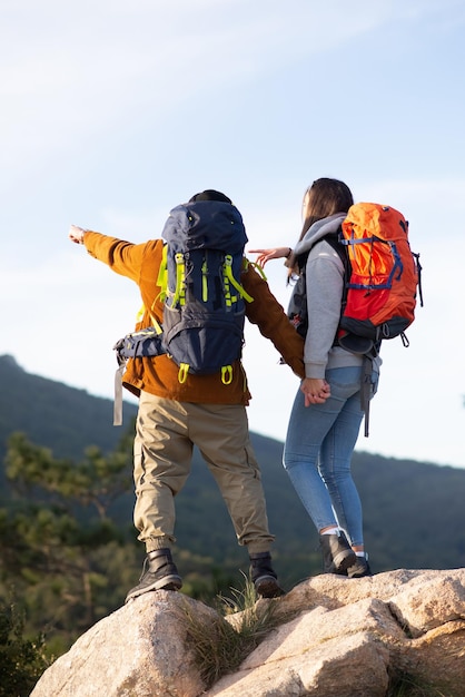 Back view of active friends hiking. Man and woman in casual clothes with hiking ammunition, pointing. Nature, activity, hobby concept