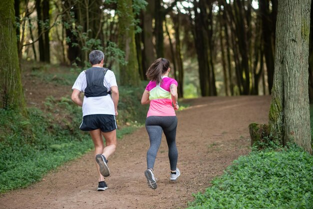 森でジョギングしているアクティブな男性と女性の背面図。屋外で運動するスポーティーな服を着た2人のスポーティーな人々。スポーツ、趣味のコンセプト