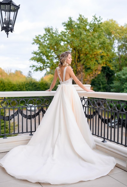 Back view of adorable female model with stylish make up and hairdo which decorated by jewelry wearing in bridal dress with long